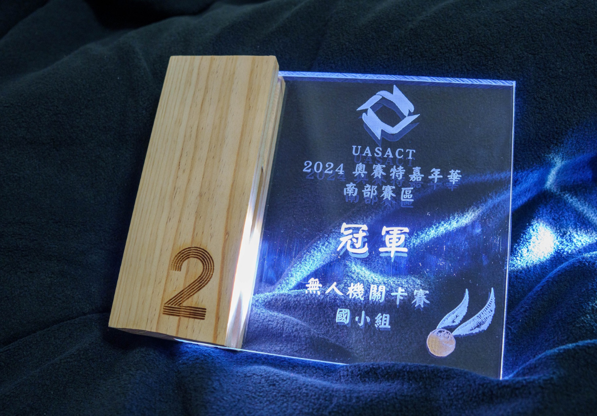 UASACT 2024奧賽特嘉年華南部賽區國小組冠軍獎狀。透明壓克力獎牌搭配木製底座，底座刻有數字2。獎狀上印有UASACT標誌、中文文字與金牌圖案。