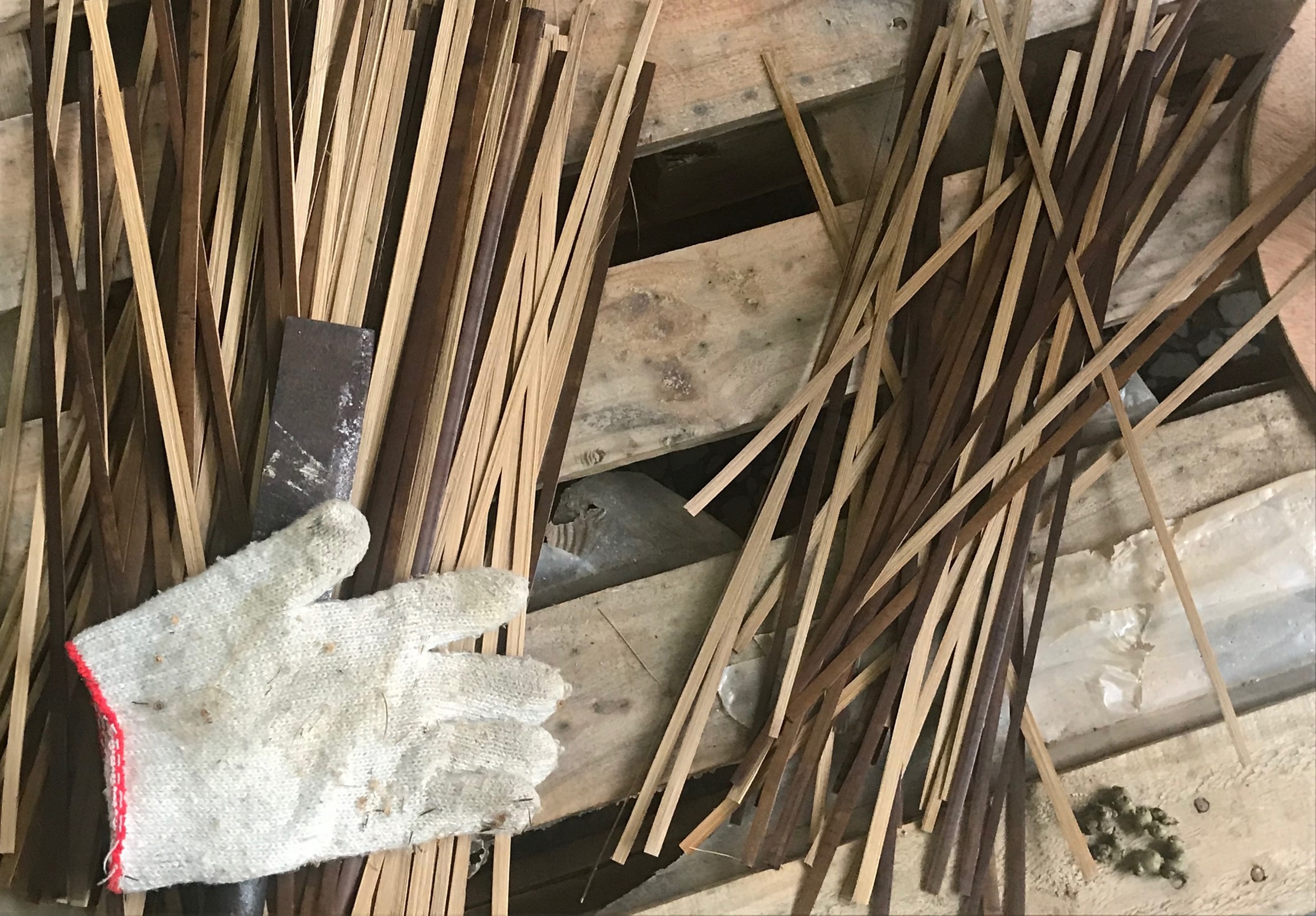 工人穿著灰色手套持黑色鏟子，在堆積的木板和建築廢料中進行清理工作。木板散亂堆放，地面為混凝土，呈現施工現場的整理場景。